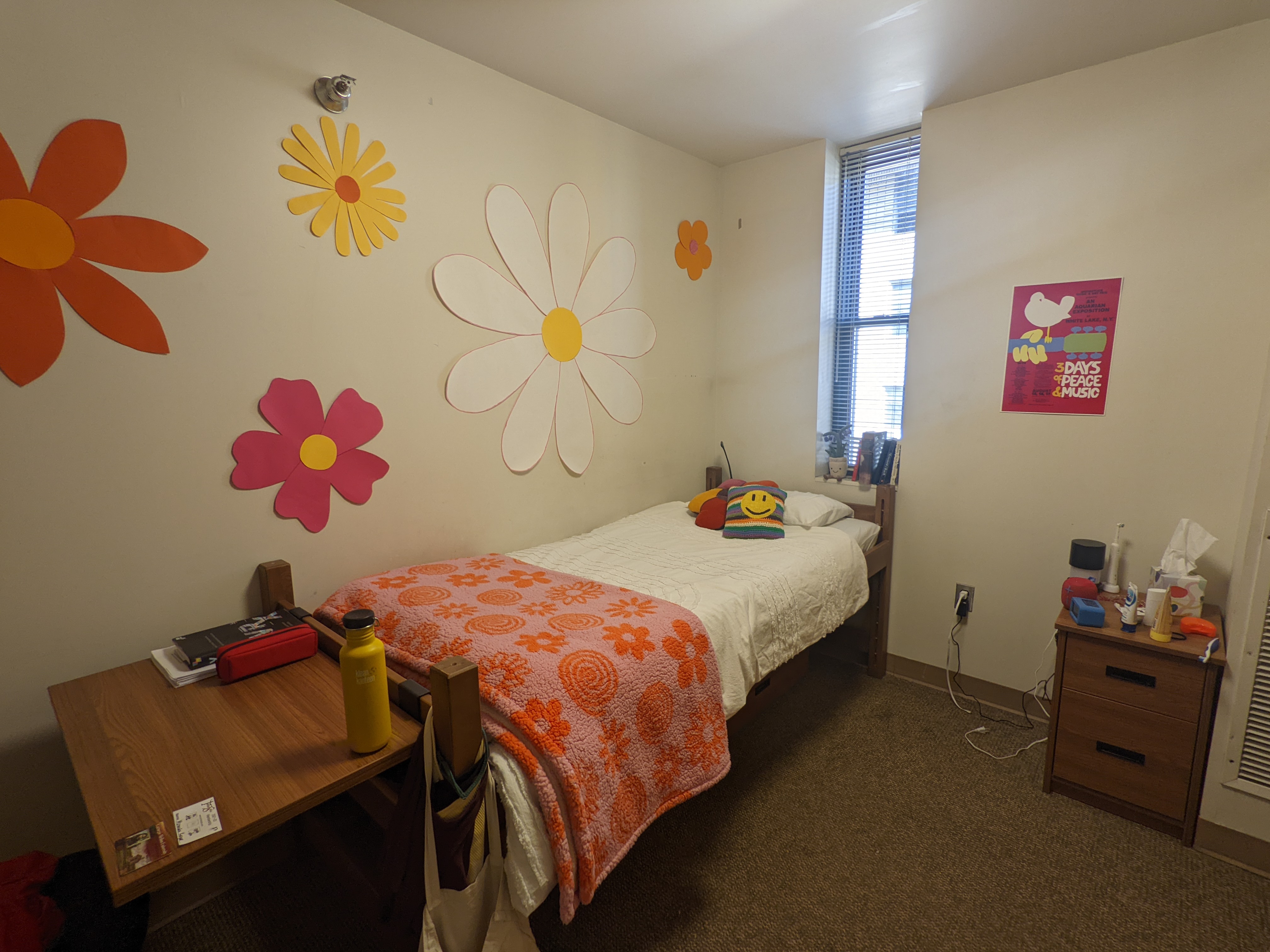 Corner view of a 60s/70s inspired dorm room with warm colors, a woodstock poster and flower-power decals on the wall